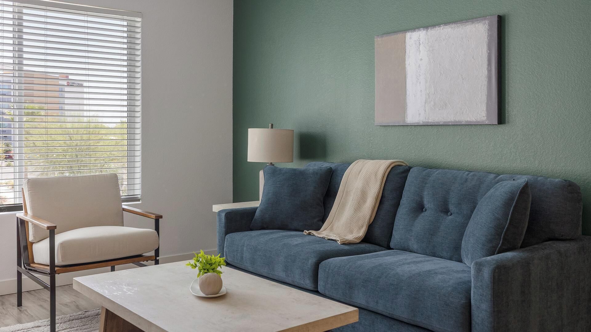 Un salon avec un canapé, un fauteuil, une table, une lampe et un tableau accroché au mur.
