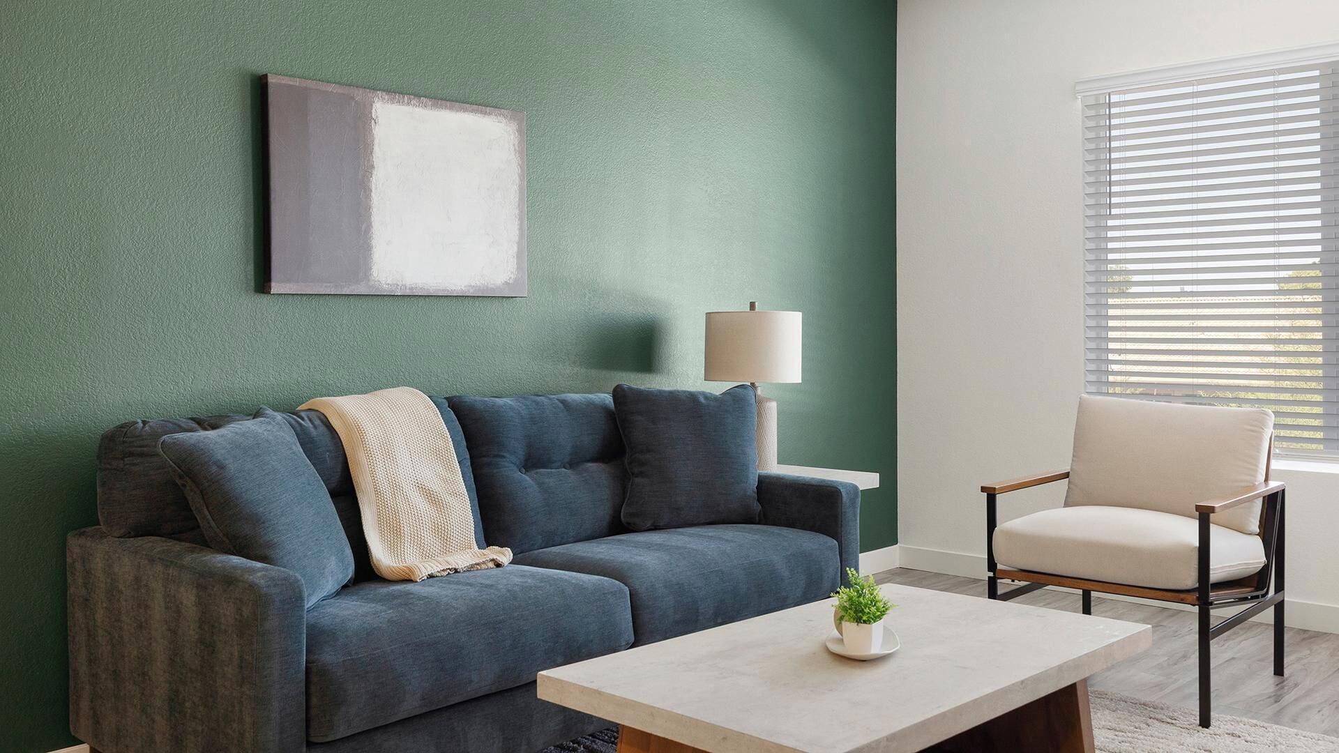A living room with a sofa, a chair, a coffee table, a lamp, and a window with blinds.
