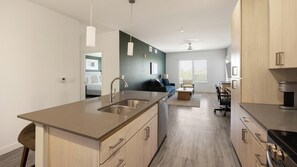 A modern kitchen with a central island, a dining area with a sofa, and a view of the living room. - Landing | Incredible 2BD, Gym, Pool (Mesa)