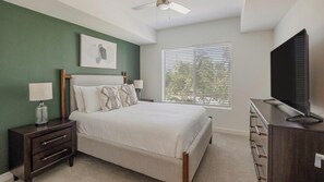 Ein Schlafzimmer mit einem Bett, Nachttischen, einer Kommode, einem Deckenventilator und einem Fenster mit Jalousien.
