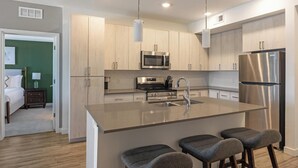 A modern kitchen with a central island, stainless steel appliances, and a green accent wall. - Landing | Modern 2BD, Gym, Pool (Mesa)
