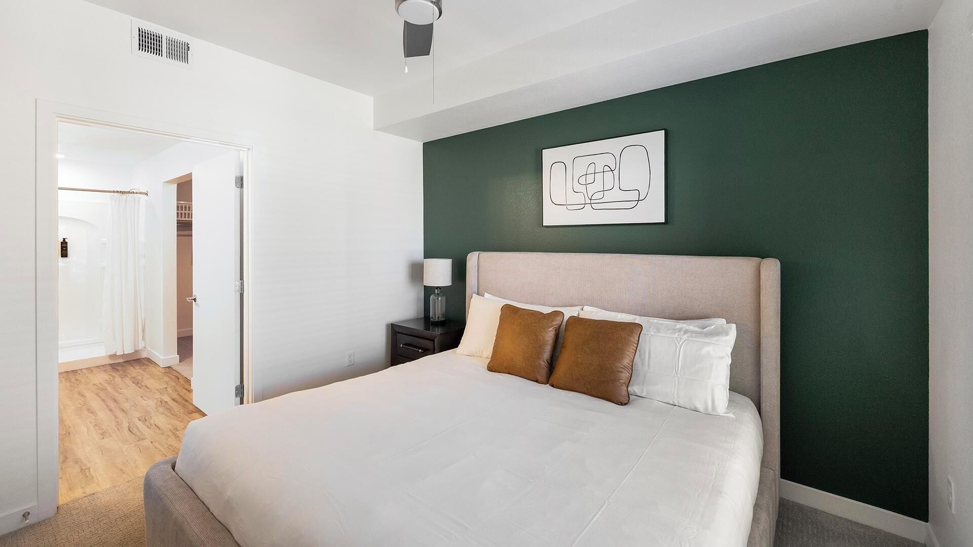 Ein Hotelzimmer mit Bett, Nachttisch, einem Wandbild und einer Tür zu einem Badezimmer.