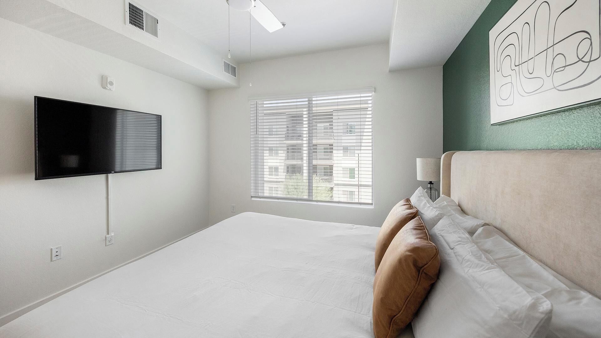 Une chambre d’hôtel moderne dotée d’un grand lit, d’un téléviseur à écran plat, d’une fenêtre avec stores et d’un mur d’accent de couleur verte.