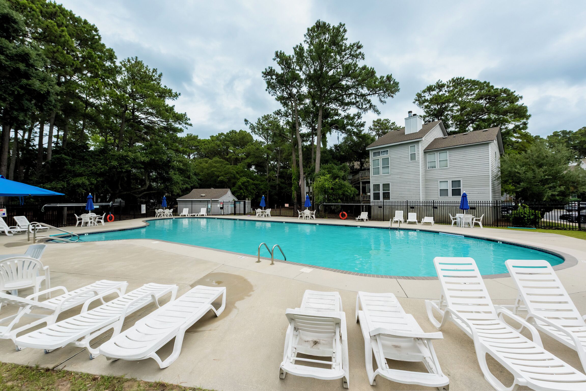 Une piscine avec des chaises longues, un poste de surveillance pour les sauveteurs et une maison en arrière-plan.