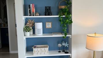 Een kamer met een blauwe wand, witte planken, een rieten bankje, een lamp en decoratieve objecten.