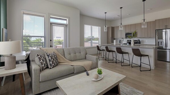 A modern living room with a sofa, coffee table, and bar stools. - Landing | Amazing 3BD, Pool, Gym (Plano)