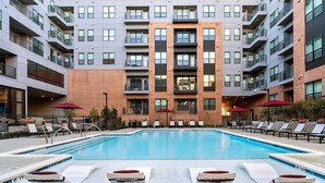 A modern building with a swimming pool, lounge chairs, and umbrellas. - Landing | Spectacular 3BD, Pool, Gym (Plano)