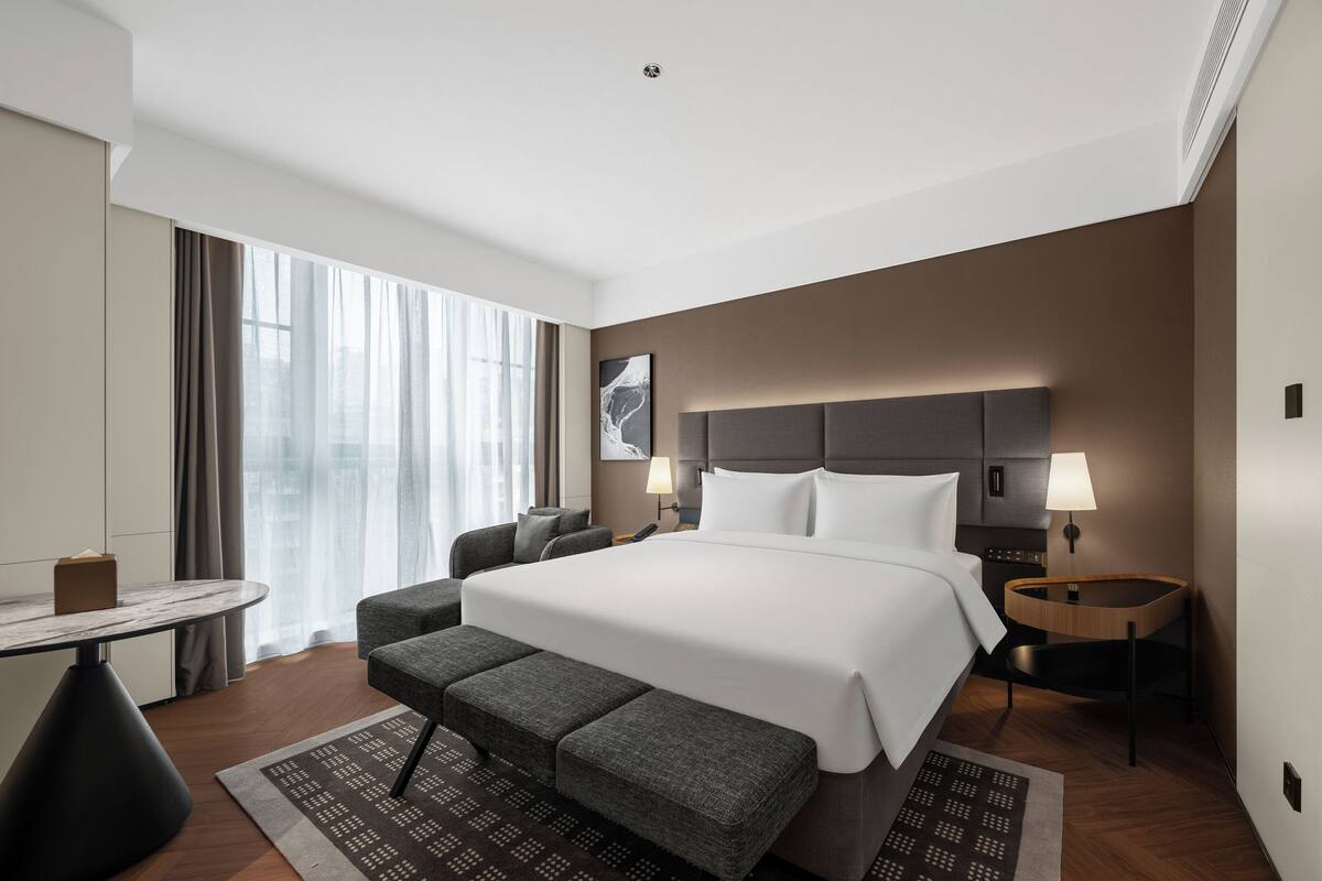 Ein modernes Hotelzimmer mit einem großen Bett, einem Schreibtisch und einer Bank.