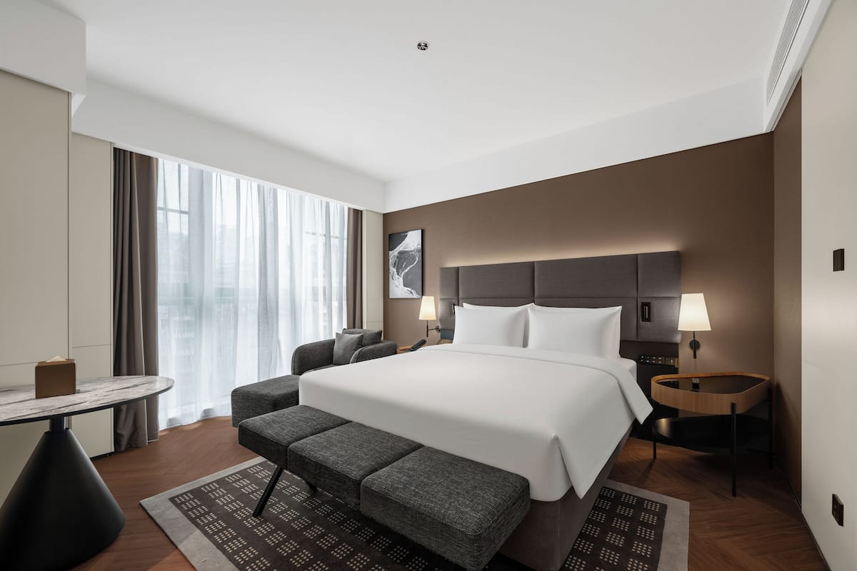 A modern hotel room with a large bed, a desk, and a bench.
