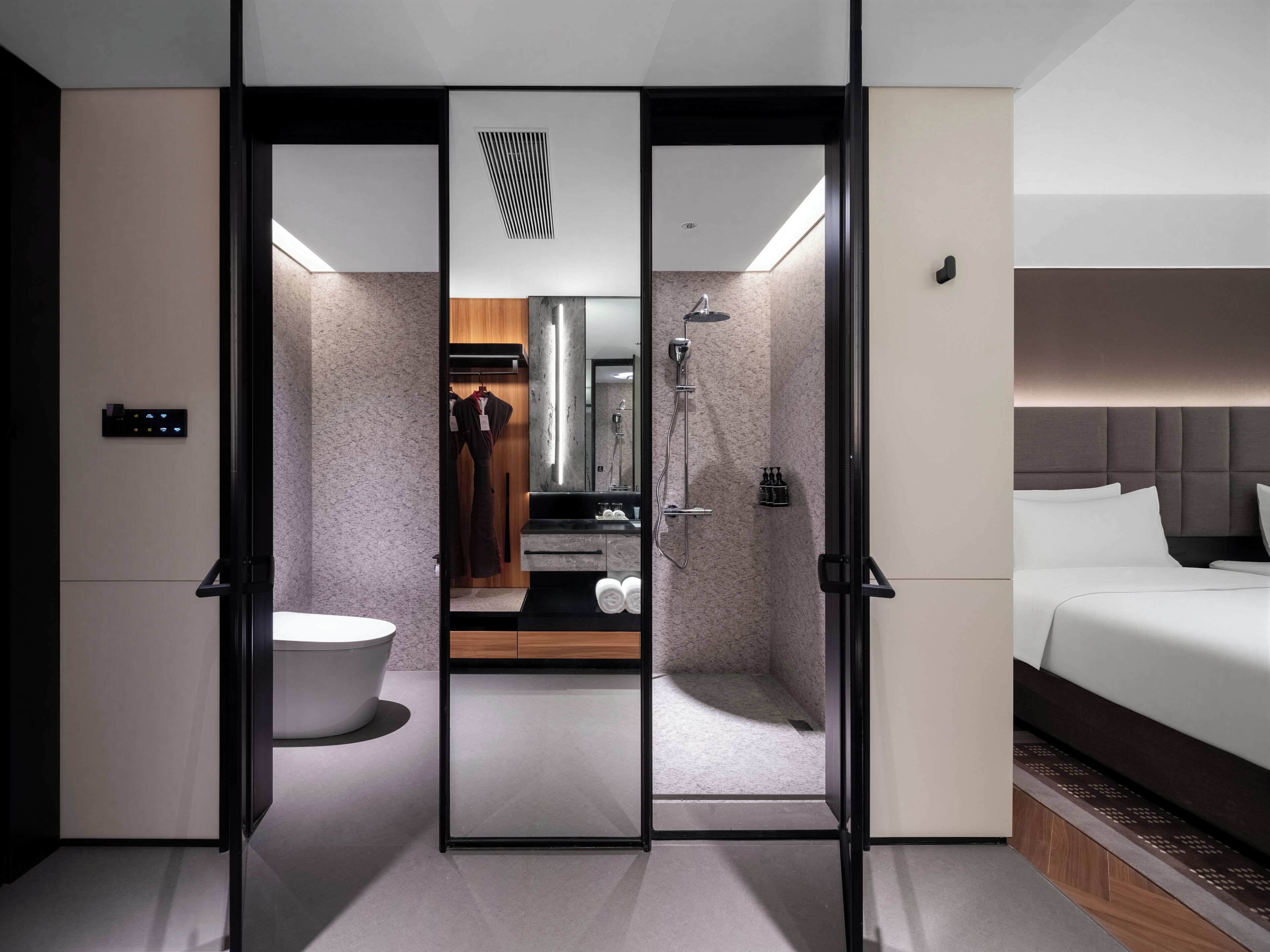 Ein modernes Hotelzimmer mit einer Schiebetür, die Bad und Schlafbereich voneinander trennt, einem großen Bett, einem Einbauschrank und einem Schminktisch mit Spiegel.
