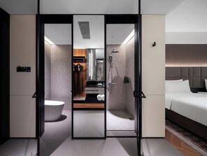 Ein modernes Hotelzimmer mit begehbarem Kleiderschrank, einem Badezimmer mit Dusche, Toilette und einem Bett.