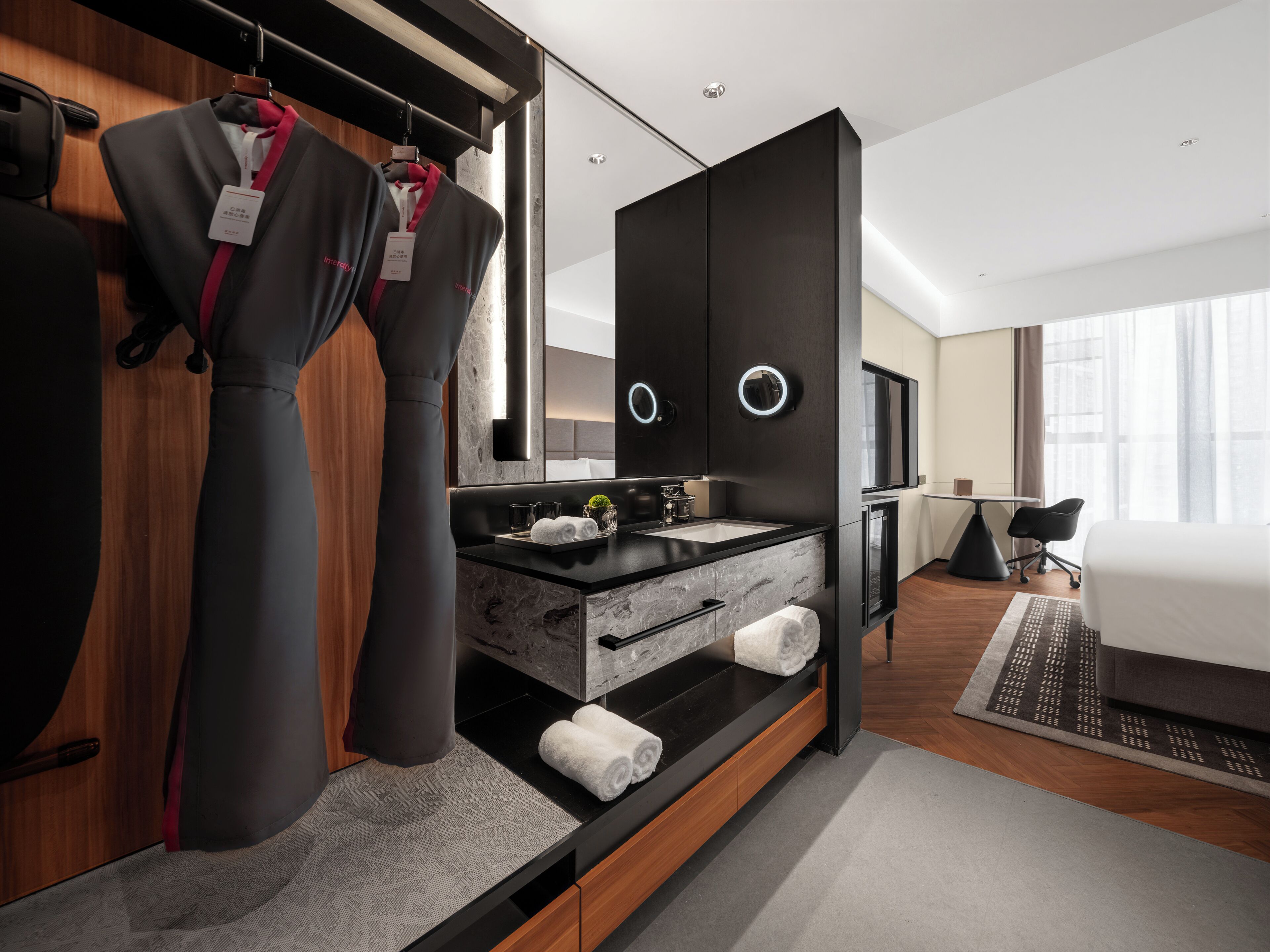 A modern hotel room with a large bed, a separate sitting area, a built-in wardrobe, and a bathroom with a marble vanity.