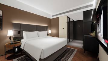 A modern hotel room with a large bed, bedside tables, a desk, and a wardrobe.