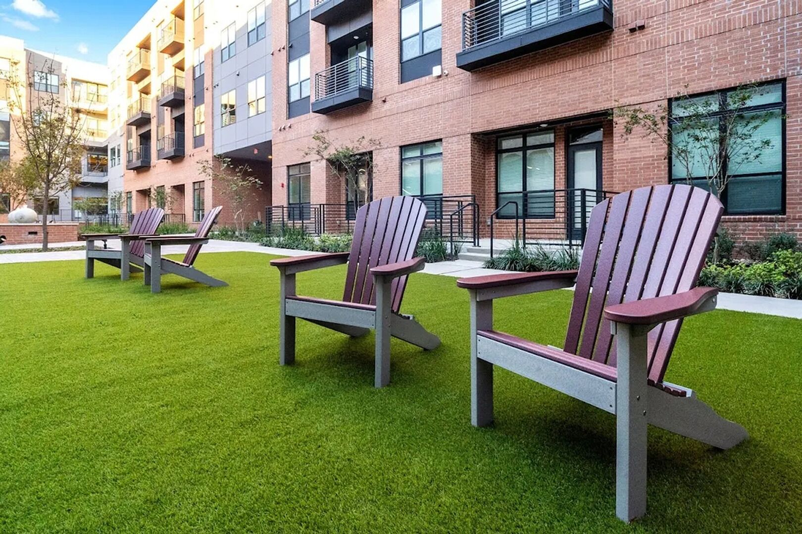 A courtyard with green artificial grass and Adirondack chairs.