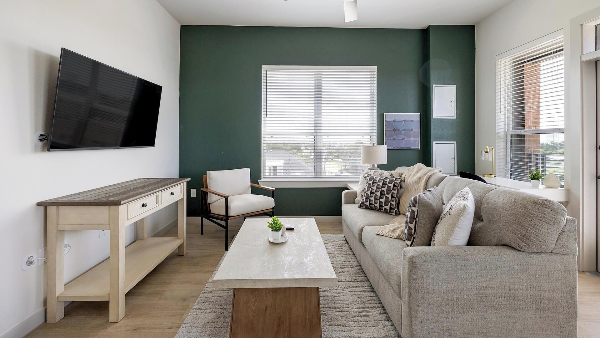 A living room with a TV, a desk, a sofa, and a window with blinds.