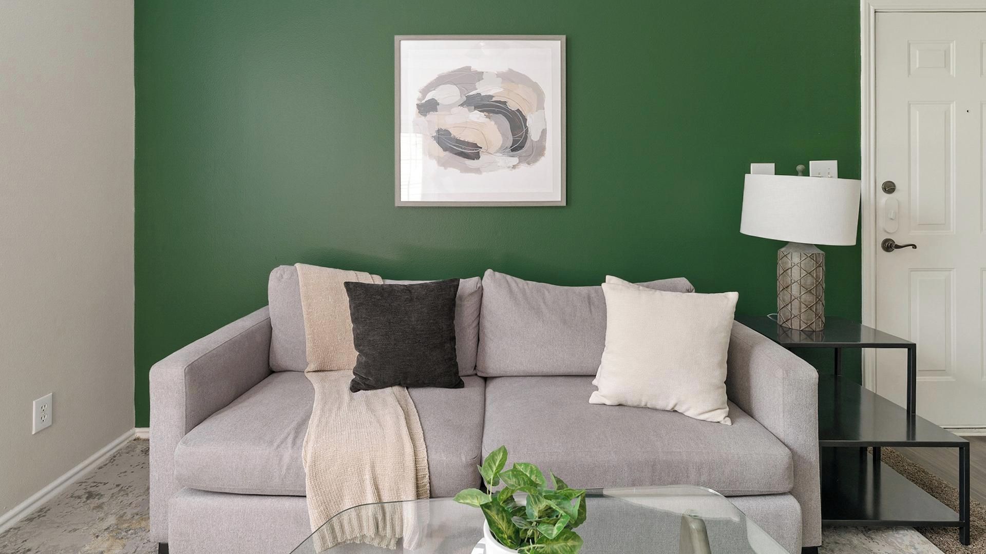 Un salon avec un canapé gris, un tableau abstrait encadré, une petite table avec une plante et une lampe posée sur une table d’appoint.
