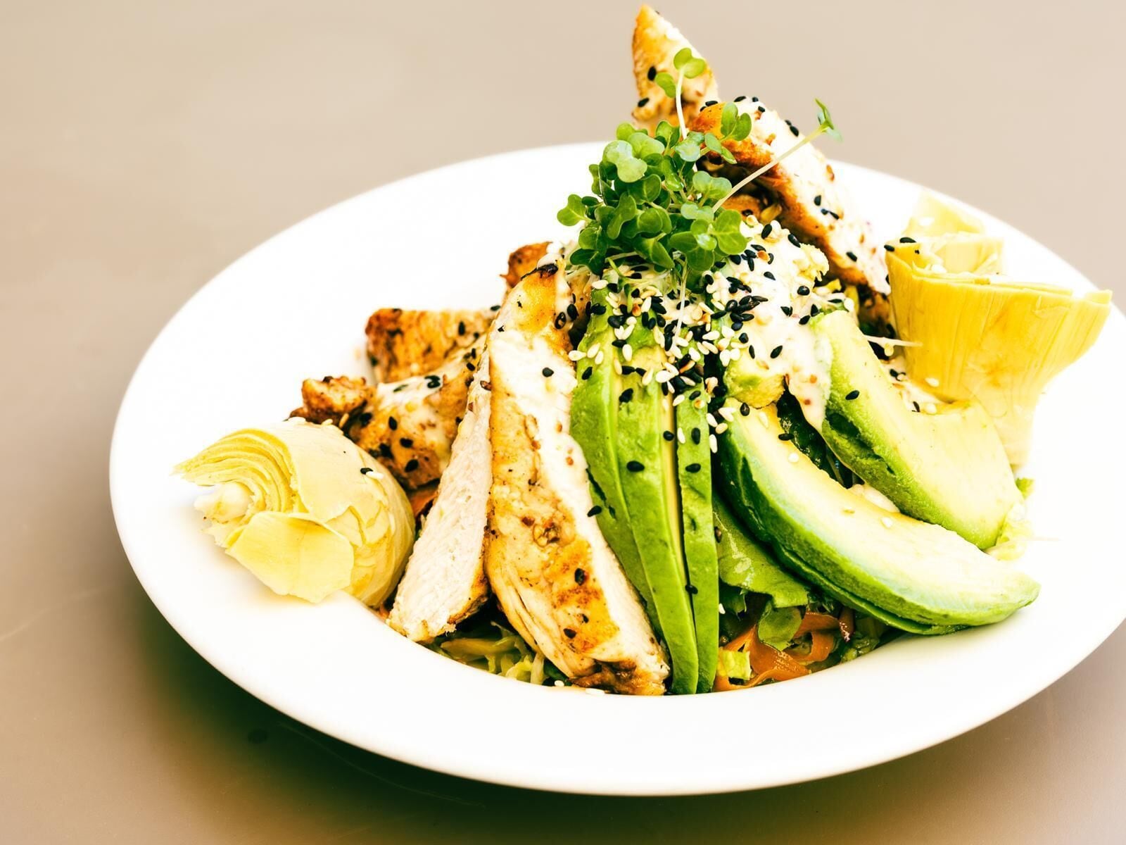 A plate of food with sliced chicken, avocado, and a lemon wedge.