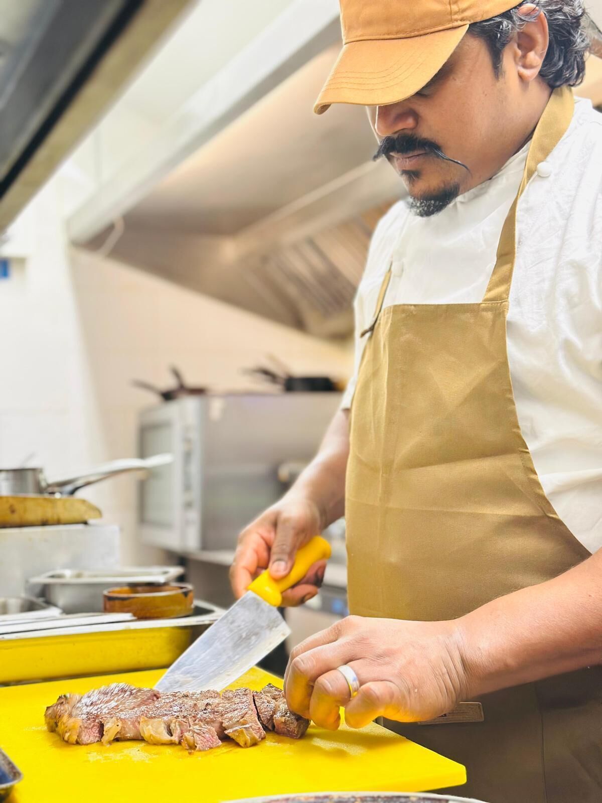 Una persona cortando un filete sobre una tabla de cortar amarilla en una cocina.