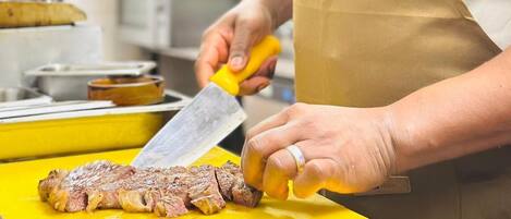 Una persona cortando un filete sobre una tabla de cortar amarilla en una cocina.