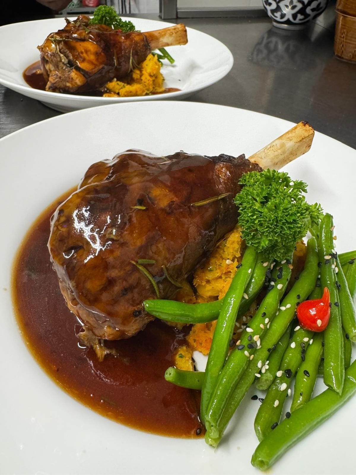 Une assiette contenant un plat de viande laqué, des légumes verts et un piment rouge.