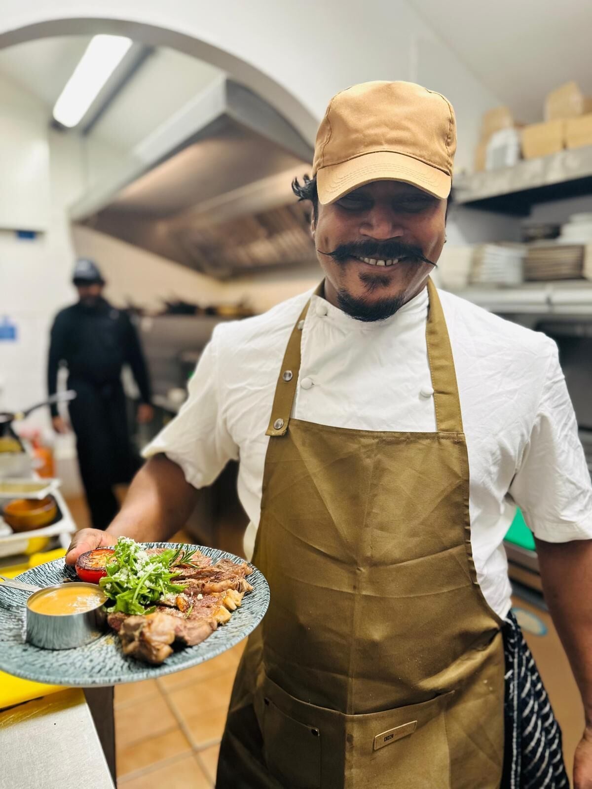 A chef holding a plate of food in a kitchen.