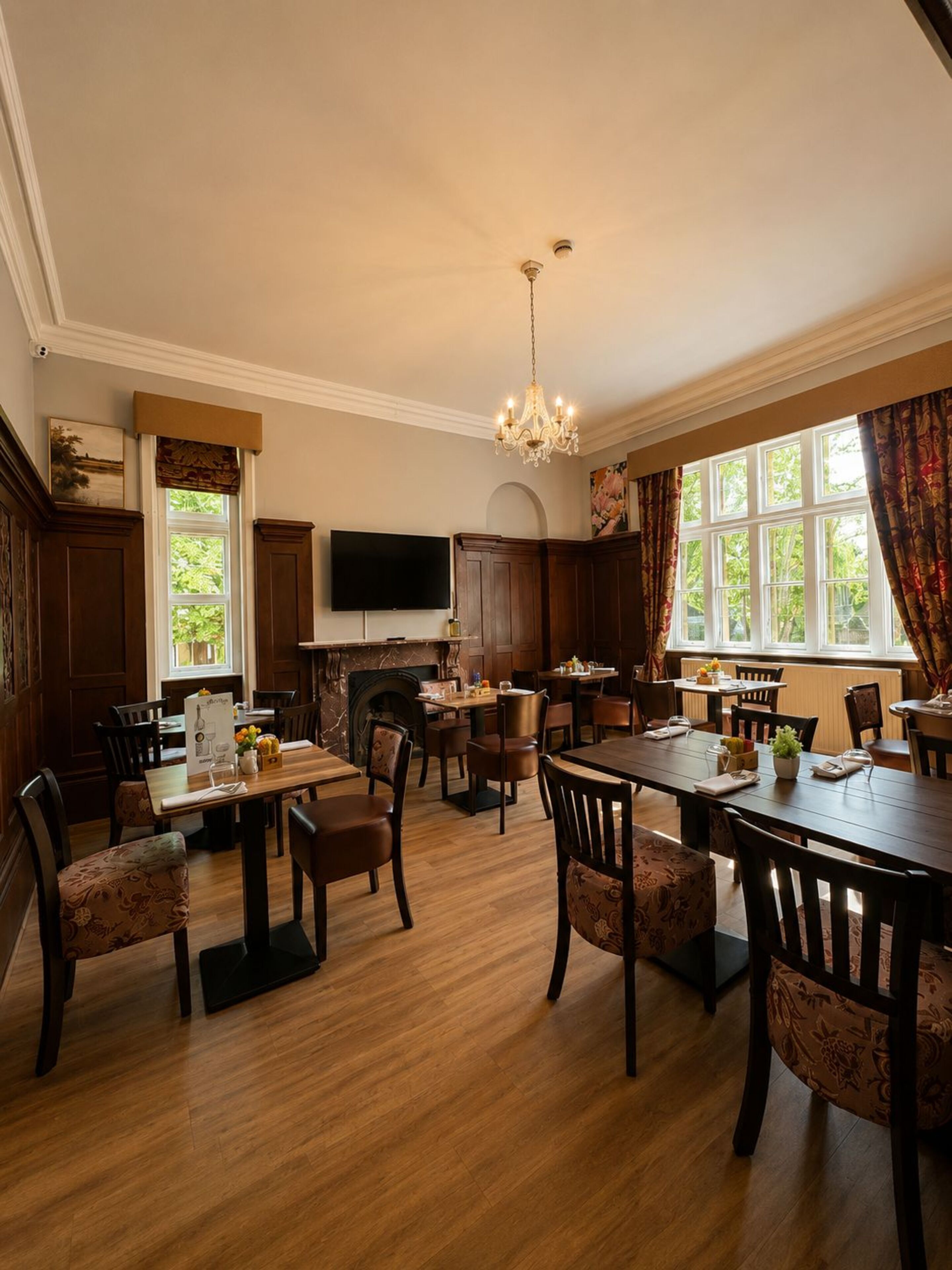 A dining area with wooden tables and chairs, a chandelier, and a fireplace.