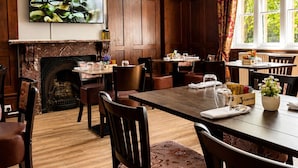 A dining area with wooden furniture, a fireplace, and a large window with curtains. - Belvilla at Brackley, near Silverstone Circuit (Brackley)