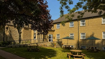 A courtyard with picnic tables and umbrellas, a stone building with a door, and a brick pathway.