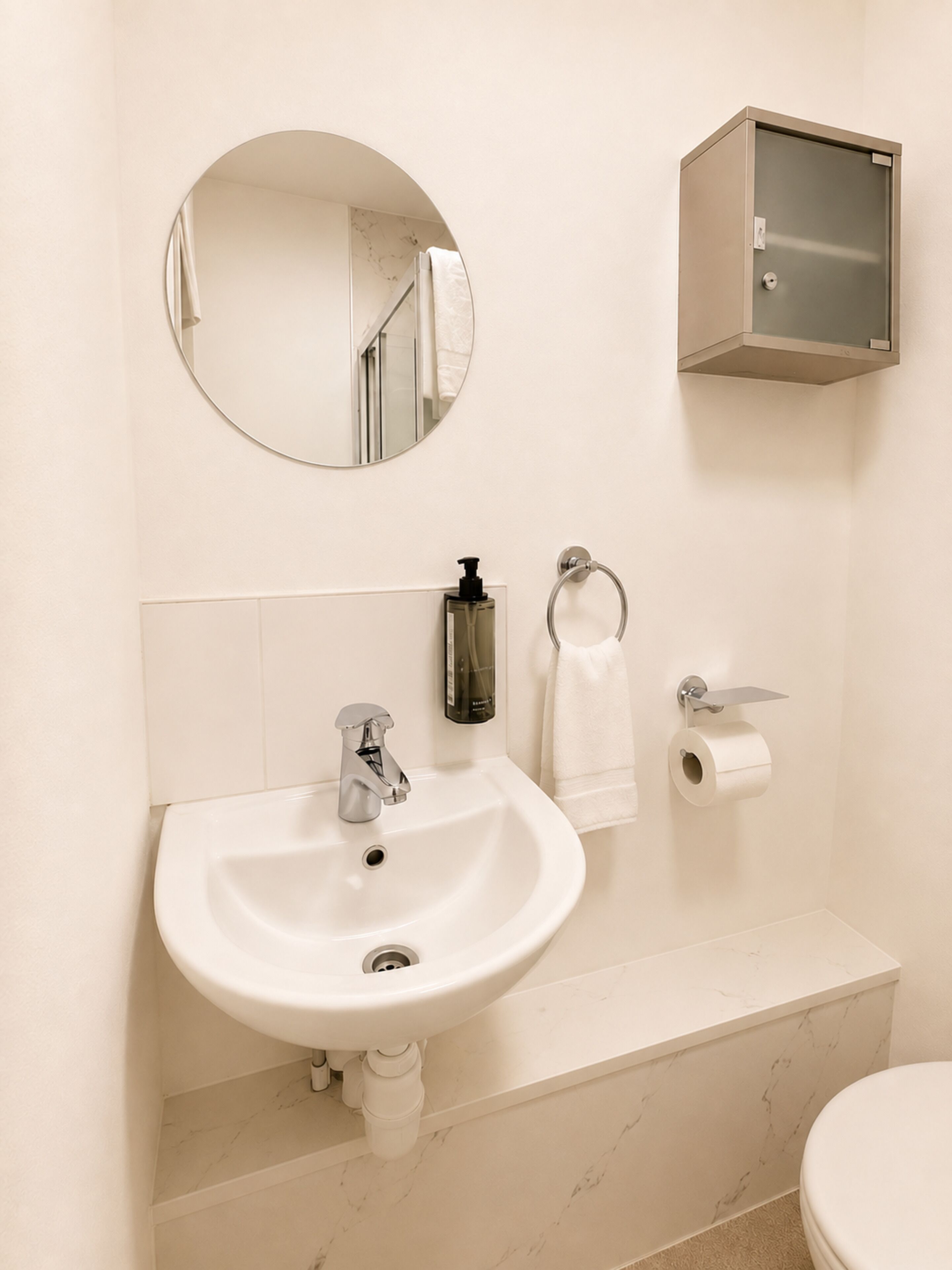 Un baño con lavamanos, espejo, papel higiénico y un armario.