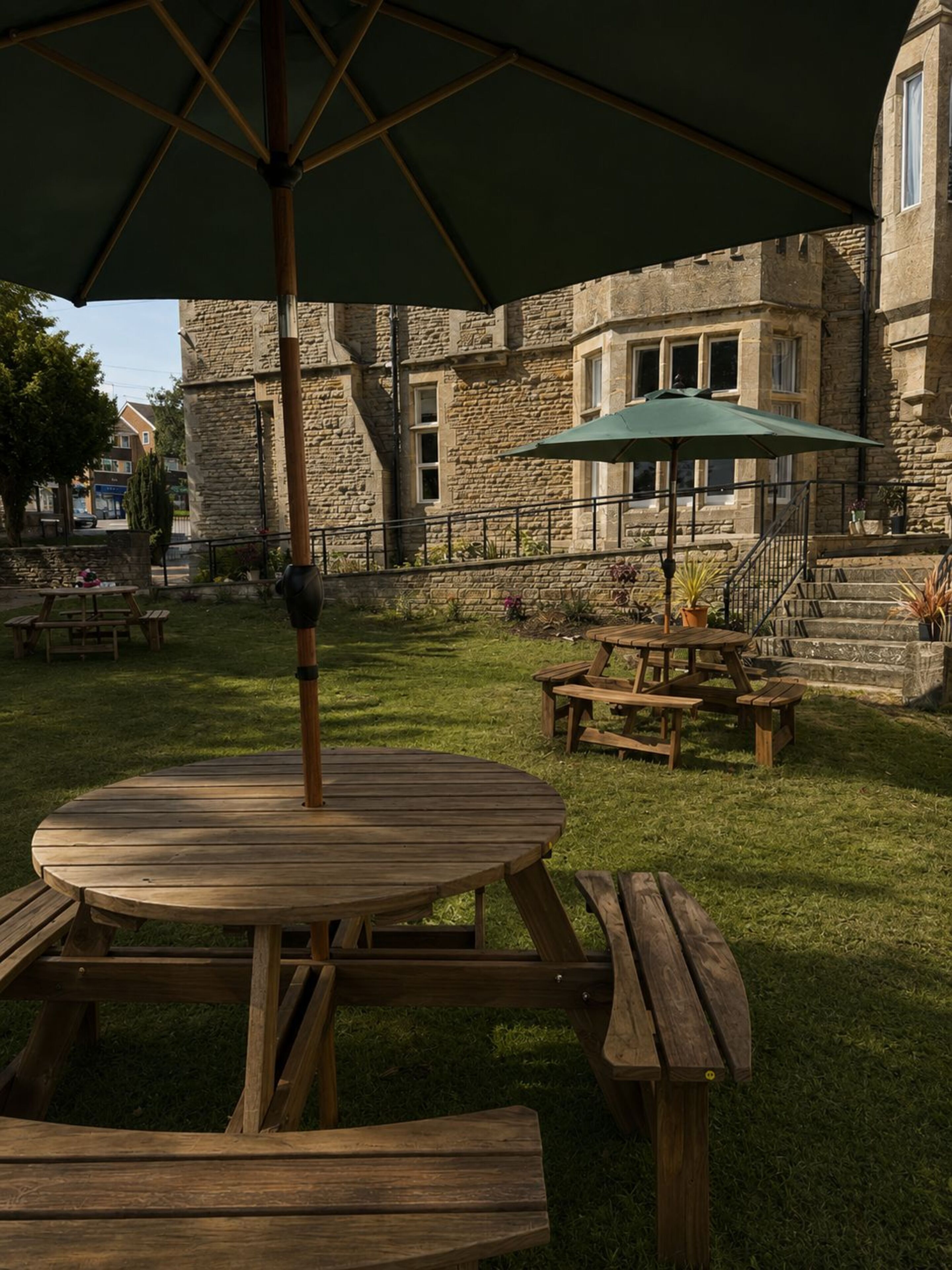 A courtyard with a stone building, picnic tables, and a wooden table with an umbrella.