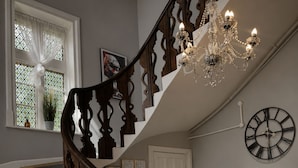 A staircase with ornate wooden railings, a chandelier, a wall clock, and a reception desk with a welcome sign. - Belvilla at Brackley, near Silverstone Circuit (Brackley)