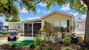 A mobile home with a screened porch, green landscaping, and a golf cart parked in front.