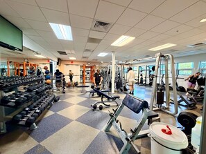 Ein Fitnessraum mit diversen Trainingsgeräten, einem Schachbrettmuster-Boden und großen Fenstern.