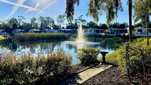 A serene lakeside setting with a fountain, surrounded by lush greenery and mobile homes.