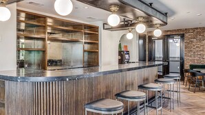 Un espace bar moderne doté d’un comptoir central, de tabourets de bar et d’un coin salon avec un banc recouvert d’un tissu vert.