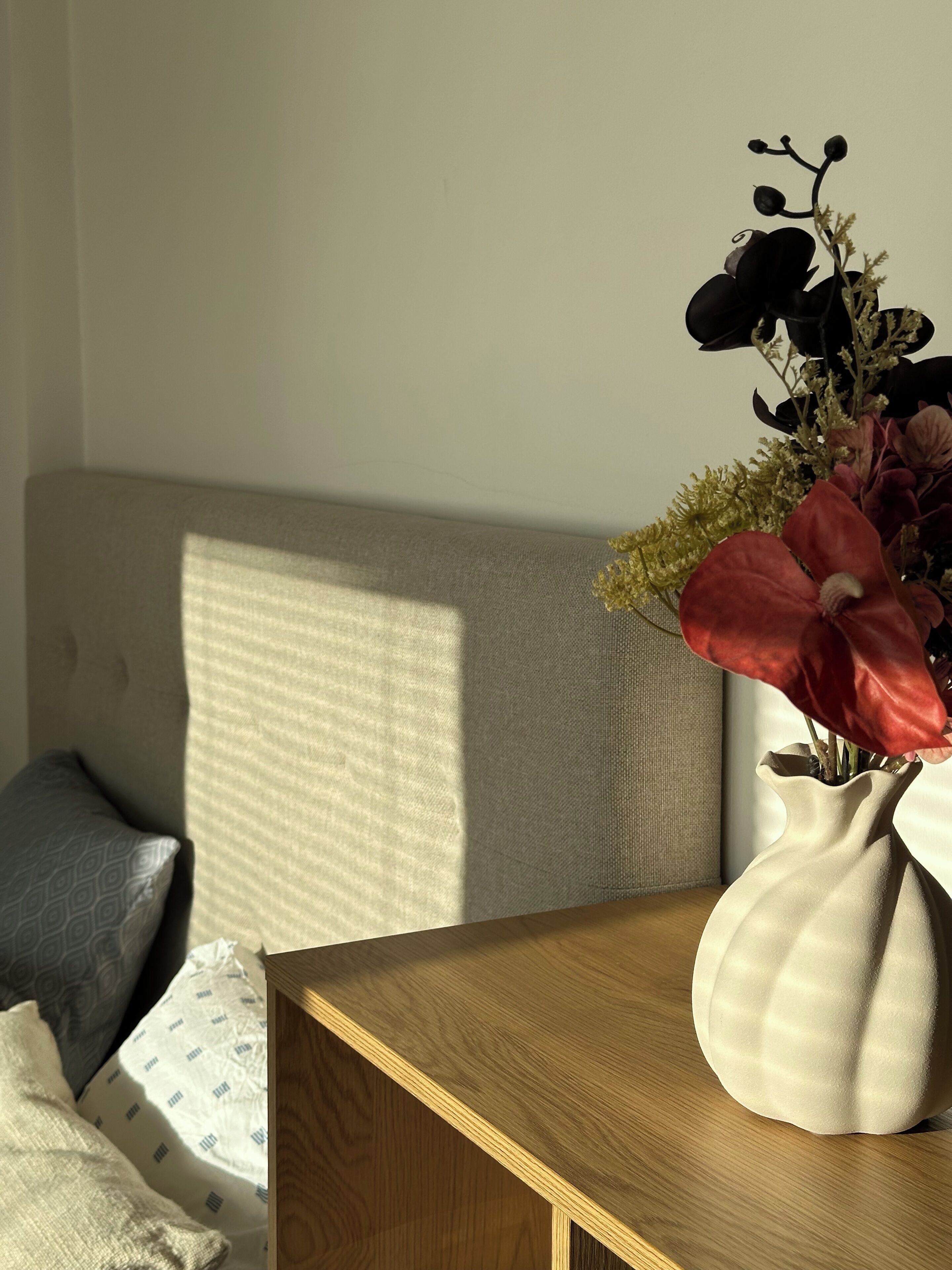 Une pièce avec une table en bois, un canapé beige et un vase rempli de fleurs.