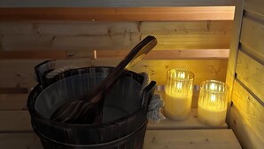 Een sauna met een houten bank, een zwarte emmer en twee brandende kaarsen.