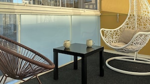 Een balkon met een hangstoel, een kleine tafel en een rieten stoel.