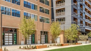 Un edificio de varios pisos con amplias ventanas, mobiliario exterior y un césped bien cuidado.