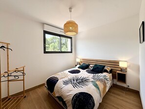 Ein Schlafzimmer mit Bett, Fenster, Holz-Kopfteil, Pendelleuchte und einer Holzablage.