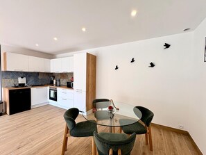 Eine moderne Küche mit weißen Schränken, einer Holz Arbeitsplatte und einem Essbereich mit einem Glastisch und vier Stühlen.
