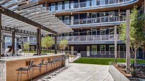 En modern byggnad med ett takförsett utomhusområde med sittplatser, en pool och en välskött gräsmatta.