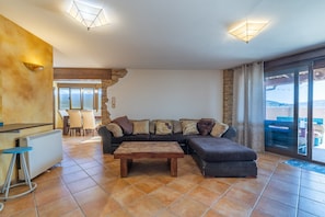 Ein Wohnzimmer mit Ecksofa, Holztisch, Barbereich und einer großen Schiebeglasdoor zum Außenbereich.