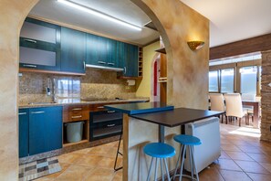 Eine moderne Küche mit blauen Schränken, einer zentralen Kochinsel mit Sitzgelegenheiten, einer Wand mit Steinverkleidung und Blick zum Essbereich.