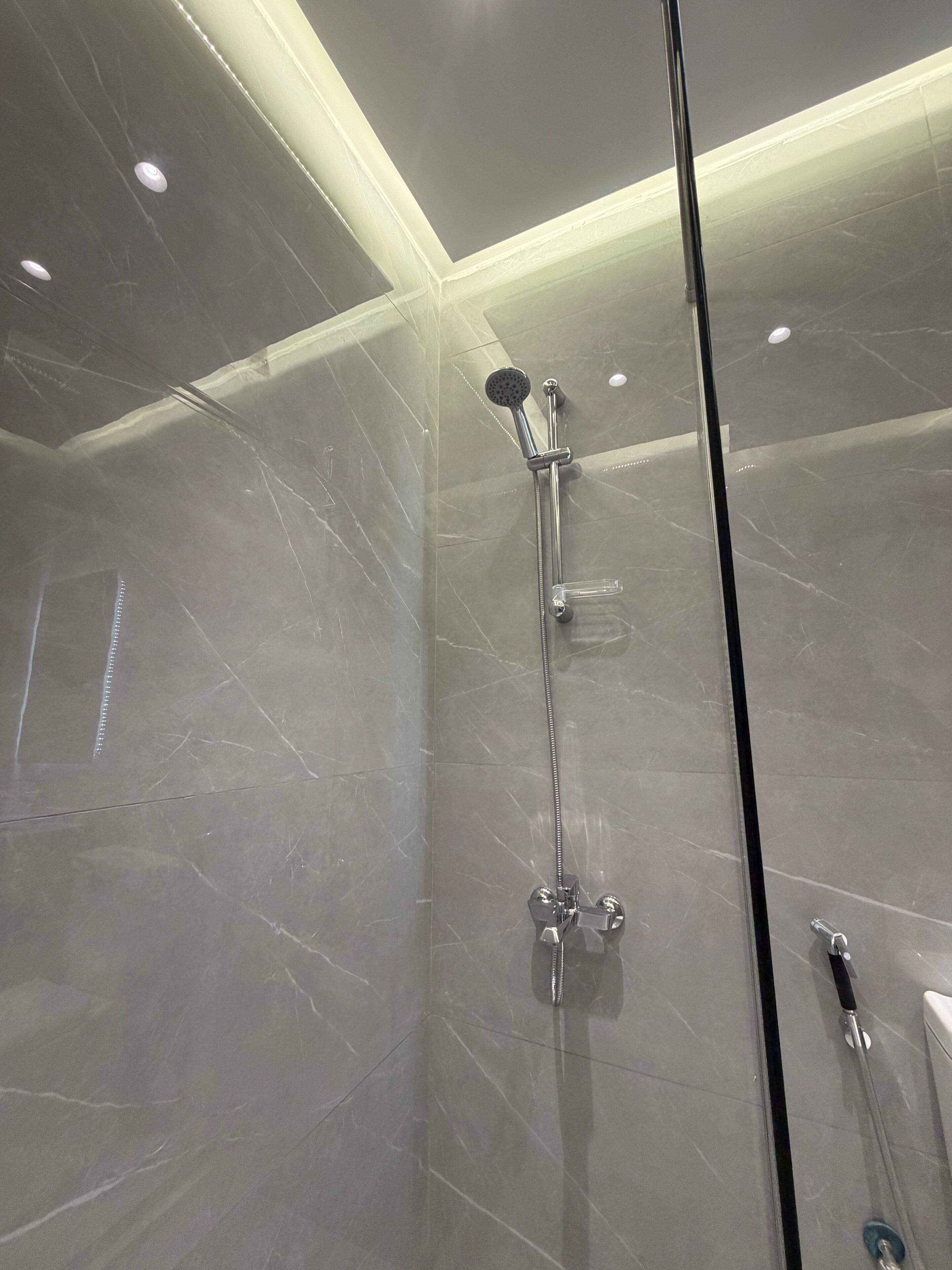 Una ducha moderna con puerta de cristal, cabezal de ducha de mano y grifo empotrado.