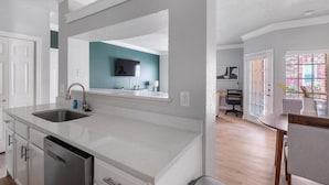 A modern kitchen with a dishwasher, double sink, and a dining area with a table and chairs. - Landing | Amazing 1BD, Clubhouse (Houston)