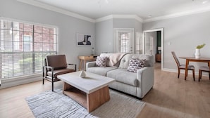 A modern living room with a sofa, coffee table, and dining table. - Landing | Amazing 1BD, Clubhouse (Houston)