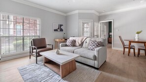 A modern living room with a sofa, coffee table, and dining table. - Landing | Stylish 1BD, Clubhouse (Houston)