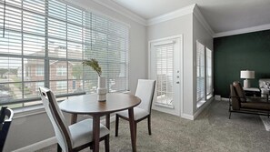 A room with a dining table, chairs, a vase with a plant, and a view through large windows. - Landing | Chic 1BD, Clubhouse (Houston)