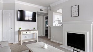 A living room with a fireplace, a television, a dining table, and a kitchen area in the background. - Landing | Chic 1BD, Clubhouse (Houston)